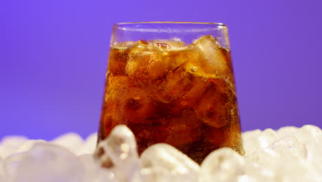 Nahaufnahme-Einer-Person,-Die-Gekühltes-Kaltgetränk-In-Ein-Glas-Auf-Eiswürfel-Vor-Violettem-Hintergrund-Gießt